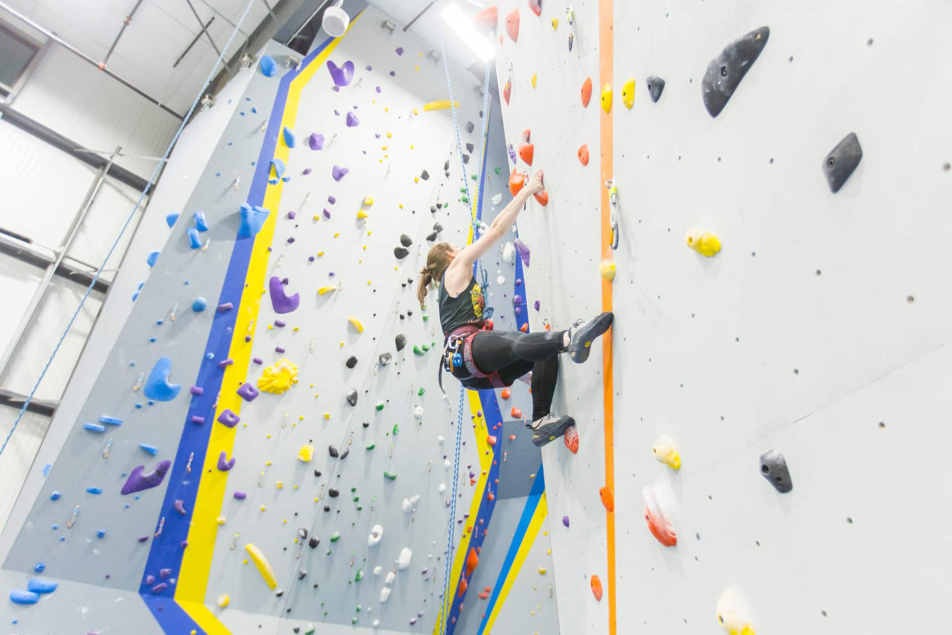 A woman climbs dynamically on top rope and uses her flagging foot to propel herself to the next hold.