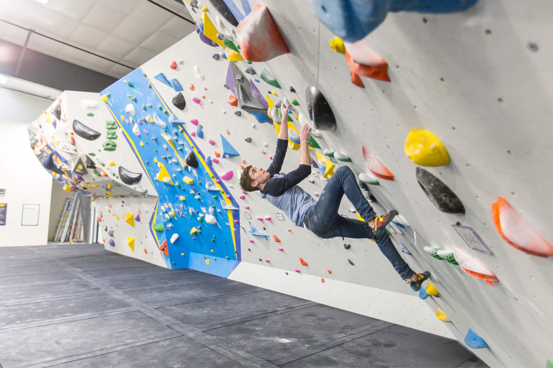 A man is bouldering on the steep part of the wall and stepping up high with his foot.